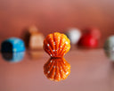 Close-up of a small orange shell shaped bon bon on a reflective surface with blurred colorful bon bons in the background.