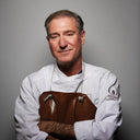 Norman Love wearing a white chef's coat and brown apron against a gray background