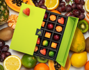 Box of chocolates with a green box surrounded by fruits on a white background