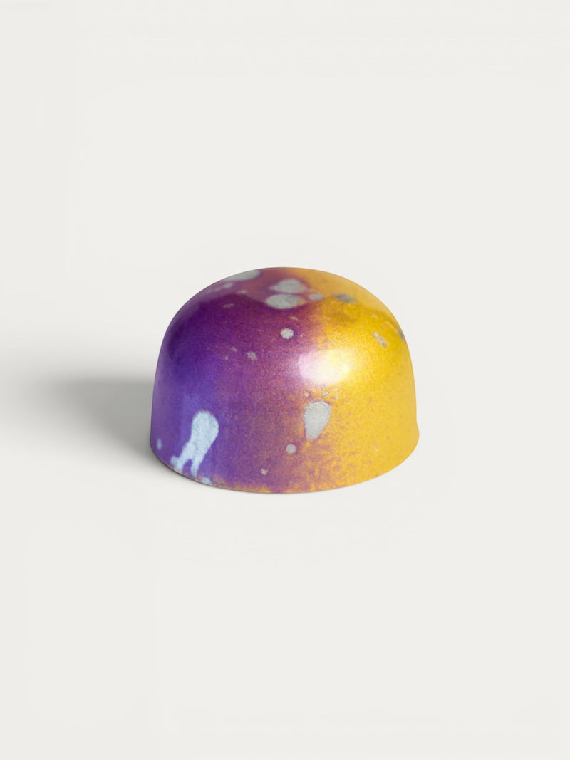 Norman Love Confections Caramel Passion chocolate with purple and gold marbled shell and white splatters.