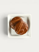 Norman Love Confections Dark Chocolate Caramel Pecan Turtles, two round chocolates with caramel drizzle.