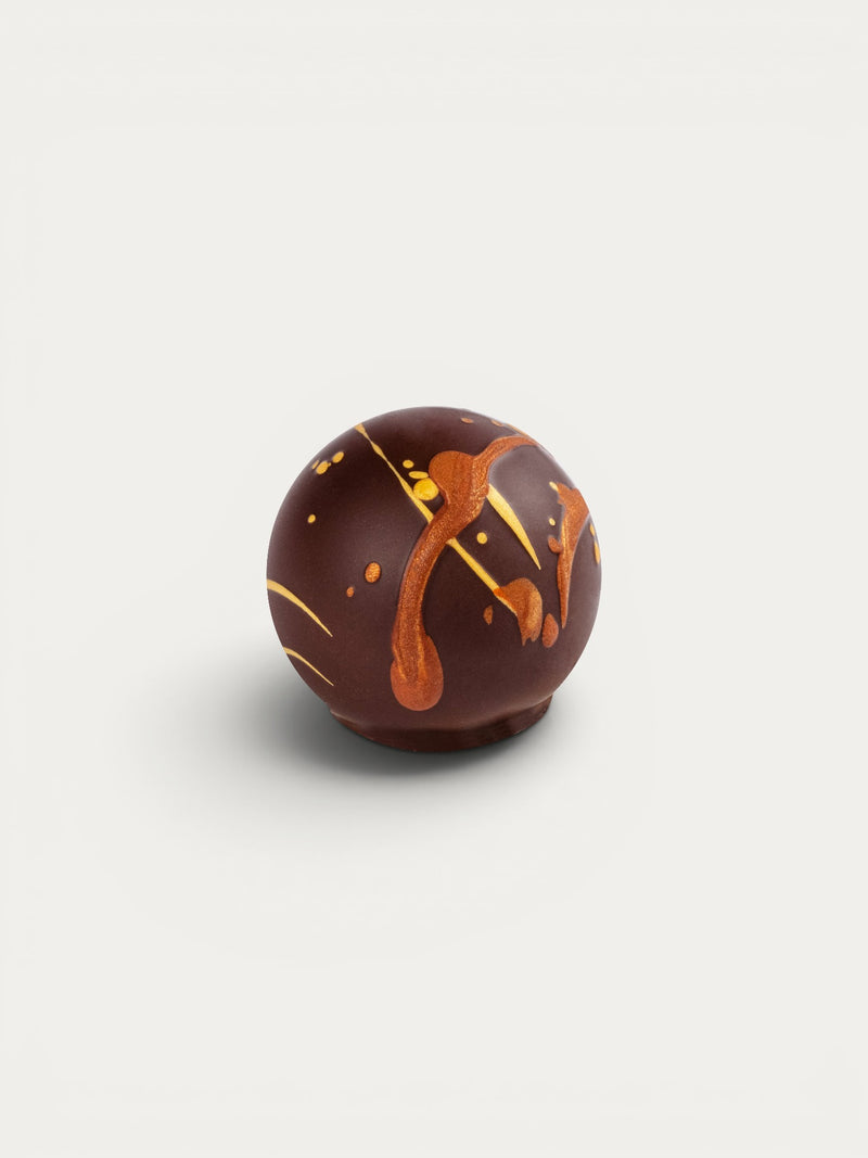 Norman Love Confections dark chocolate truffle with gold and bronze drizzles and speckles.