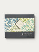 Norman Love Confections Gourmet Favorites box with a botanical print sleeve featuring blue and green leaves. Includes pecan turtles, sea salt caramels, and S'more Love chocolates.