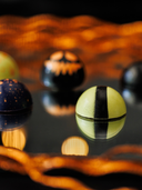 Norman Love Confections Halloween chocolate truffles in vibrant colors and spooky designs on a reflective surface.