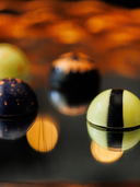 Norman Love Confections Halloween chocolates with vibrant colors and artistic designs on a reflective surface