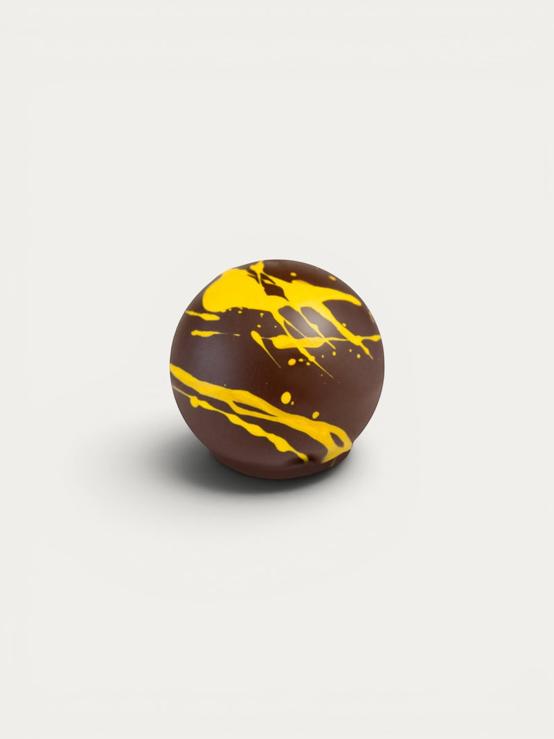 Norman Love Confections dark chocolate truffle with bright yellow ganache drizzle and splatters.
