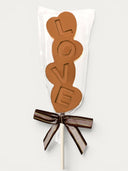 Norman Love Confections milk chocolate pop spelling LOVE, tied with a brown ribbon.