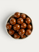 Norman Love Confections milk chocolate malt balls in a white bowl, featuring a crunchy malted center coated in smooth milk chocolate.
