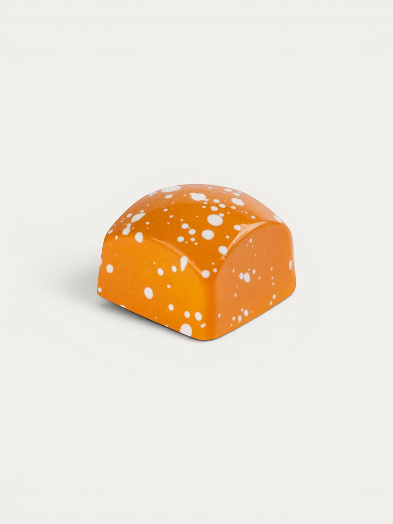 Norman Love Confections New York Cheesecake chocolate with orange glaze and white speckles.