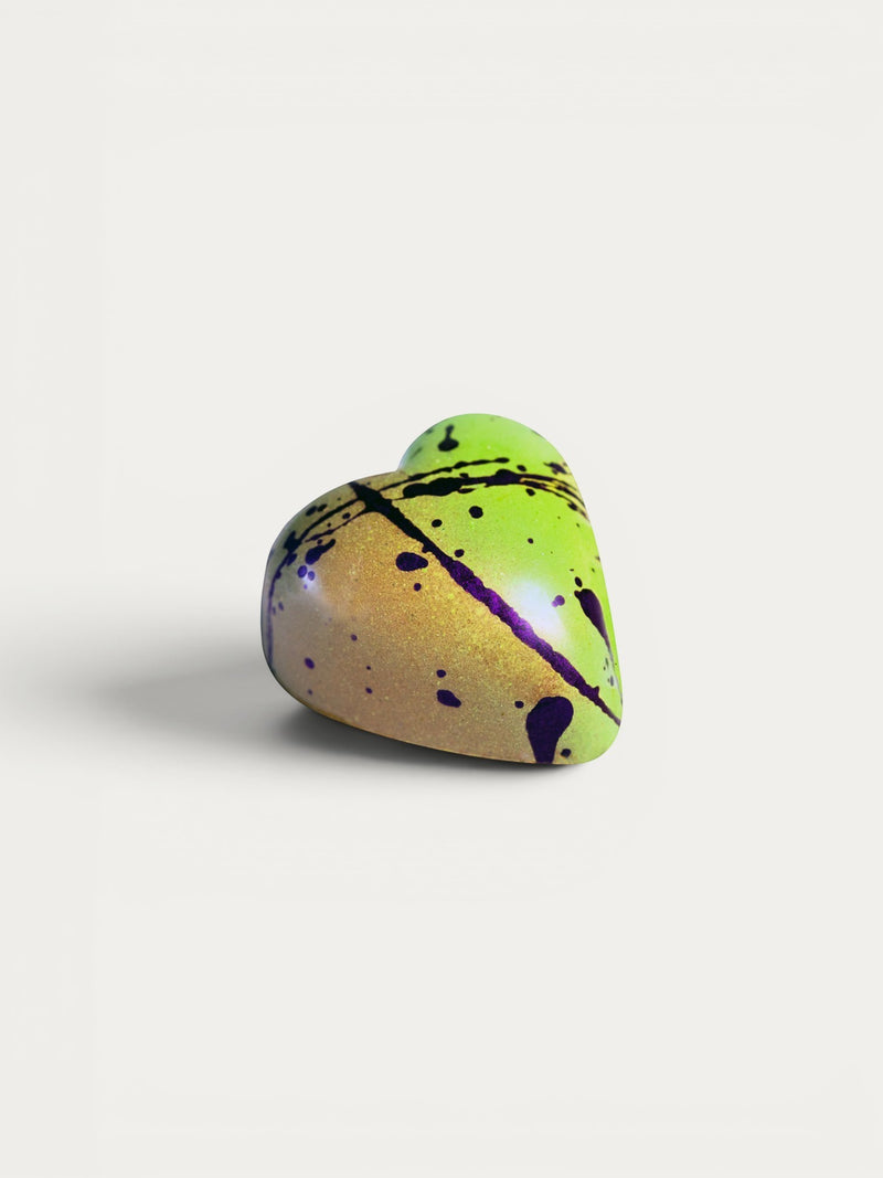 Norman Love Confections Sicilian Pistachio heart-shaped chocolate with green, gold, and purple splatter design.
